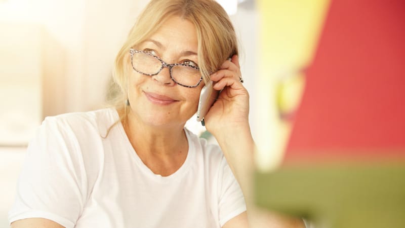 Beautiful blonde Caucasian elderly female wearing glasses having phone conversation with her old friend using electronic device, discussing latest news with cute smile on her face, sitting at home Beautiful blonde Caucasian elderly female wearing glasses having phone conversation with her old friend using electronic device, discussing latest news with cute smile on her face, sitting at home